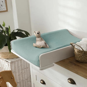 Housse de matelas à langer sauge unie installée sur une table à langer murale avec doudou ourson
