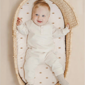 Bébé souriant allongé dans un couffin en osier sur un drap-housse en gaze de coton à motif soleil