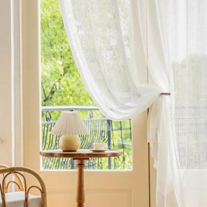 Rideau blanc noué près d'une fenêtre donnant sur un balcon verdoyant