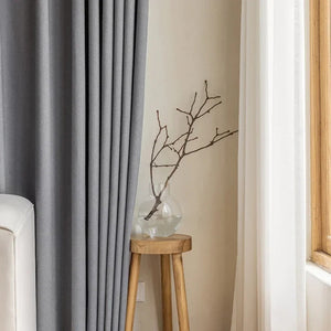 Détail du rideau gris drapé avec un vase et des branches sur une console bois