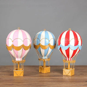 Trois ballons à air chaud en métal forgé posés sur une table en bois fond gris