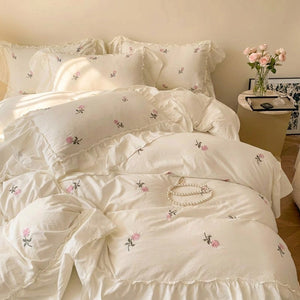 Parure de lit brodée de roses dans un coin de chambre cosy avec fleurs sur table de chevet