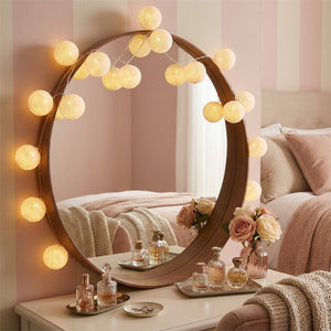 Guirlande boules de coton LED enroulée autour d'un miroir rond dans une chambre feminine tons roses