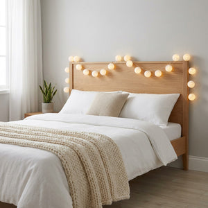 Guirlande lumineuse boules de coton blanches 6 cm accrochée au-dessus d'une tête de lit en bois dans une chambre cosy nordique