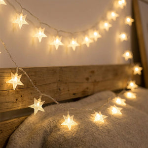 Guirlande lumineuse à étoiles LED blanc chaud illuminant une chambre cosy près d'un mur en bois