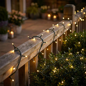 Guirlande lumineuse LED blanc chaud sur une rambarde de terrasse et un arbuste la nuit