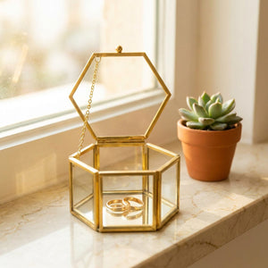 Boîte à bijoux hexagonale ouverte avec deux bagues dorées sur une étagère en marbre près d une fenêtre