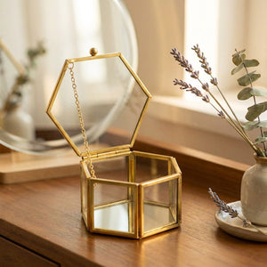Boîte à bijoux hexagonale en verre sur une coiffeuse avec un miroir rond et des fleurs séchées