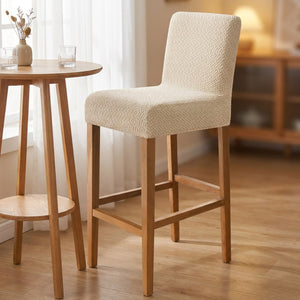 Housse de chaise de bar en jacquard beige installée sur un tabouret haut en bois dans une salle à manger chaleureuse