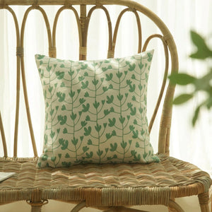 Housse de coussin verte à motif de branchages sur un fauteuil en rotin