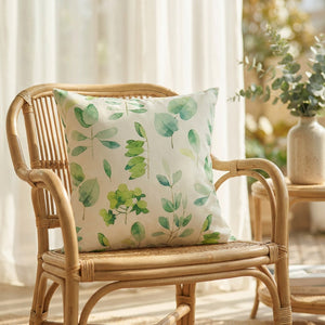 Housse de coussin imperméable verte à feuillage aquarelle posée sur un fauteuil en rotin