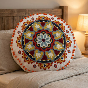 Housse de coussin ronde brodée mandala posée sur un lit contre une tête de lit en bois