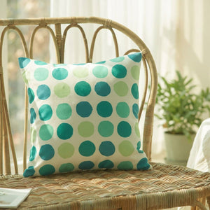 Housse de coussin à pois verts et bleu canard sur un fauteuil en rotin