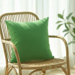 Housse de coussin vert uni sur un fauteuil en rotin