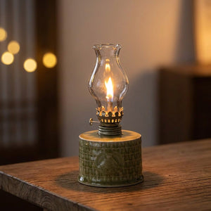 Lampe à pétrole en céramique céladon vert olive allumée sur une table en bois