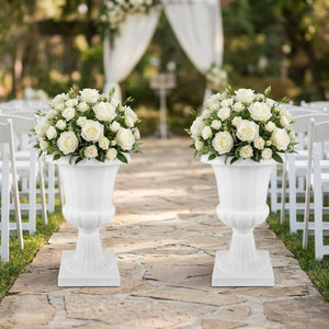 Deux vases médicis blancs fleuris de roses blanches le long d'une allée de mariage