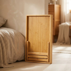 Plateau de lit en bambou aux pieds repliés rangé à plat contre un lit dans une chambre