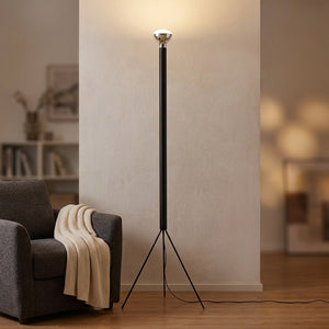 Lampadaire trépied noir allumé près d'un fauteuil dans un coin lecture cosy