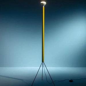 Lampadaire trépied jaune allumé diffusant une lumière chaude dans une pièce sombre