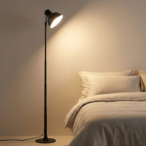 Lampadaire LED noir en version sur pied allumé dans une chambre cosy près du lit