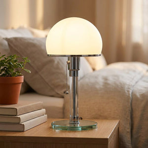 Lampe de table Bauhaus posée sur une table de chevet avec des livres et une plante