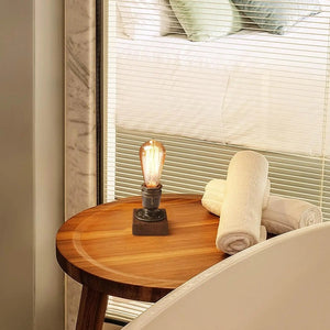 Lampe de chevet industrielle allumée sur une table près d'un lit et de serviettes