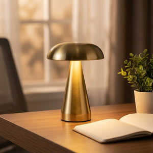 Lampe champignon dorée allumée sur un bureau en bois avec un carnet et une plante