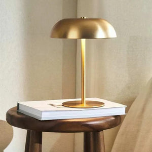 Lampe de chevet champignon dorée posée sur un livre près d'une fenêtre