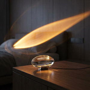 Lampe cristal ovale posée sur une console qui projette un halo doré en forme de comète sur le mur