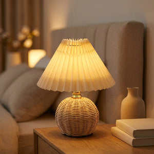 Lampe de chevet en rotin avec abat-jour plissé beige allumée sur une table de nuit