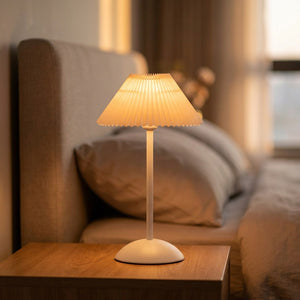 Lampe de table sans fil à abat-jour plissé blanc et pied métal allumée sur une table de nuit