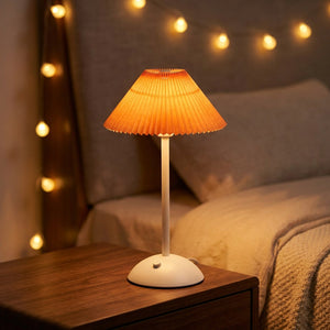 Lampe de table sans fil avec abat-jour plissé orange allumée sur une table de nuit