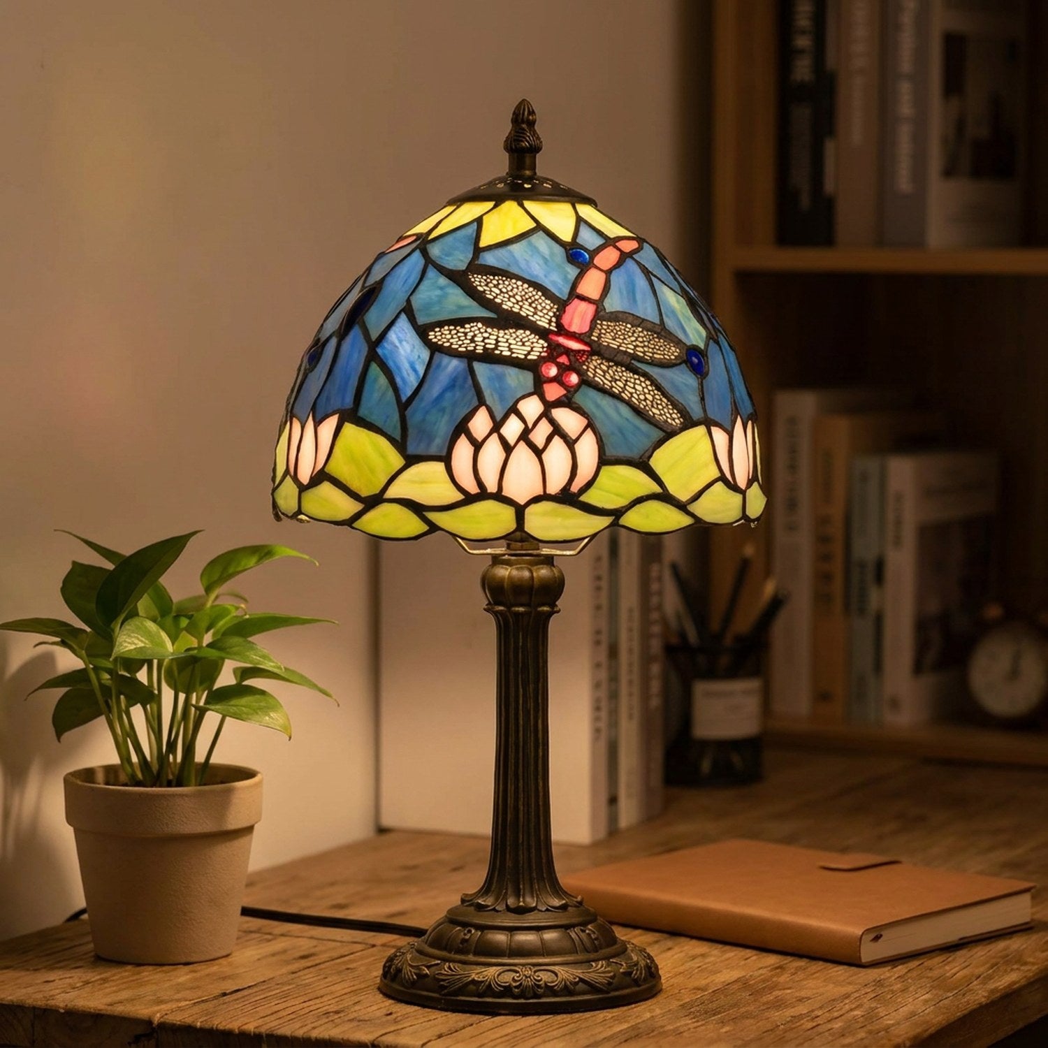 Lampe vitrail Tiffany libellule allumée sur un bureau bois avec plante verte