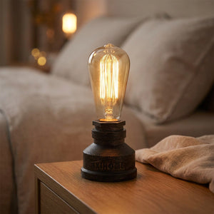 Lampe tuyau industrielle en fer bronze patiné allumée posée sur une table en bois