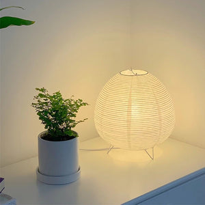 Lampe en papier de riz allumée dans un angle de pièce lumineuse avec une plante