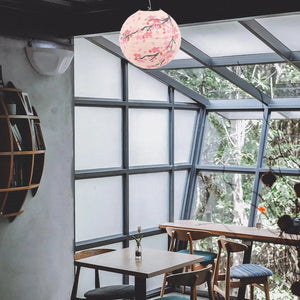 Lanterne sphérique en papier rose avec motifs sakura suspendue dans un intérieur festif