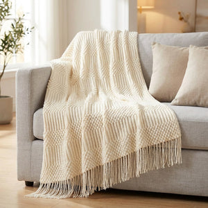 Plaid tricoté crème drapé sur un canapé en lin gris avec coussins