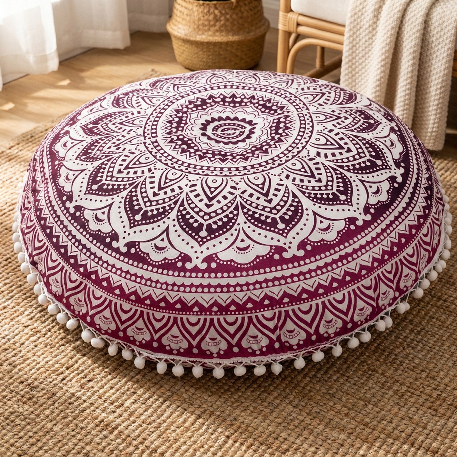 Coussin de sol mandala bordeaux posé sur un tapis en jute près d'un fauteuil en rotin