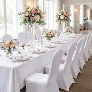 Longue table de mariage dressée avec des chaises habillées de housses blanches et bouquets roses