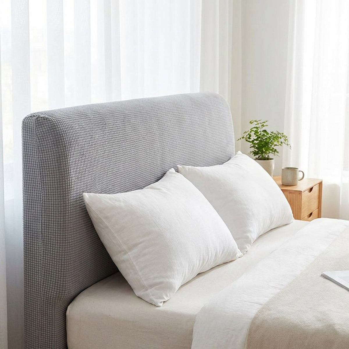 Housse de tête de lit gris clair vue de trois quarts sur un lit avec oreillers blancs