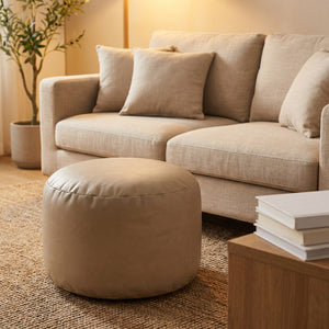 Pouf ottoman rond beige utilisé en repose-pieds devant un canapé en lin