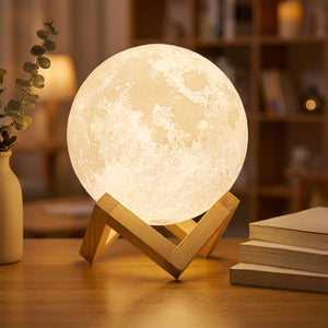Lampe lune allumée en blanc chaud sur un bureau en bois avec des livres et de l'eucalyptus