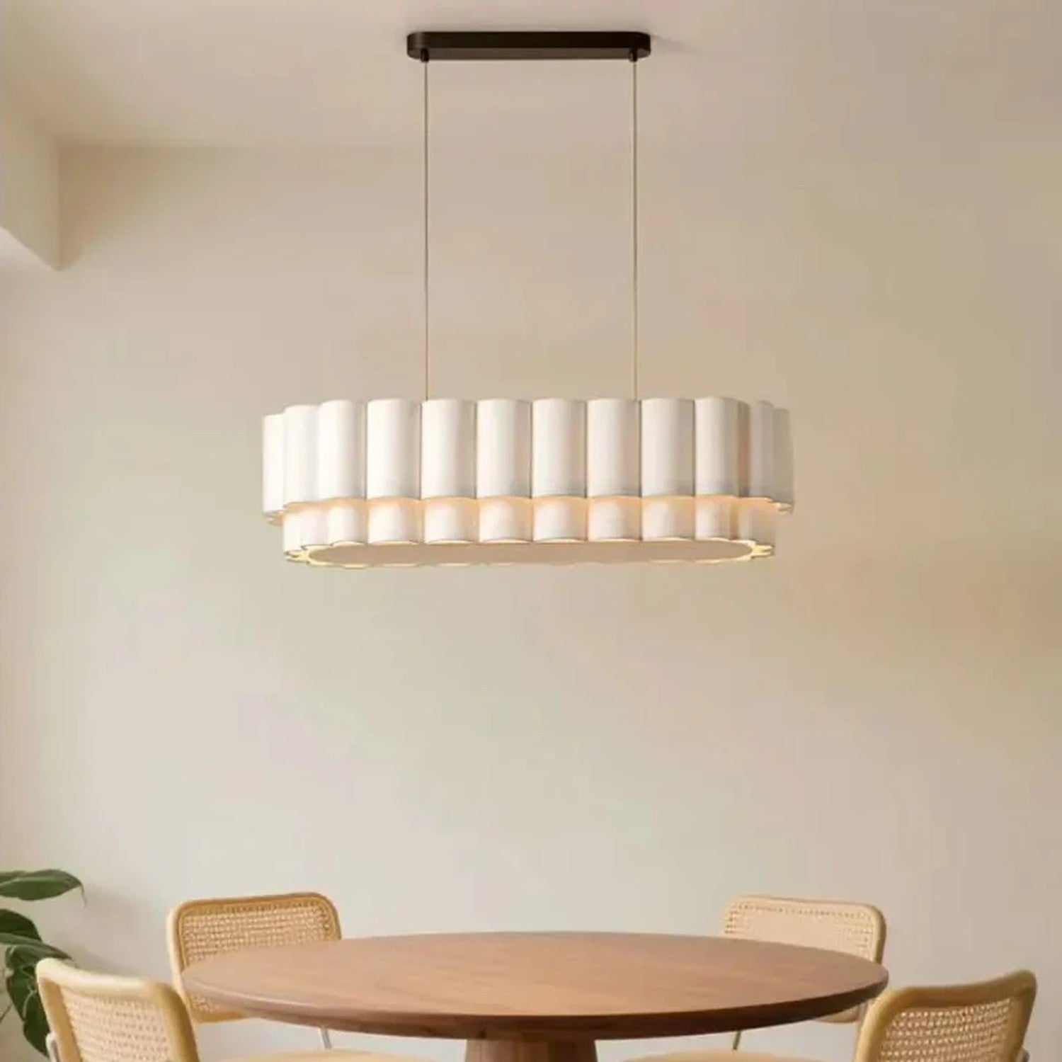 Suspension linéaire en tissu beige allumée au-dessus d'une table ronde avec chaises en rotin