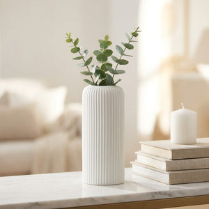 Vase blanc à rainures avec branches d'eucalyptus sur une étagère en marbre