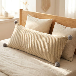 Coussin long en velours côtelé beige contre une tête de lit en bois avec coussins
