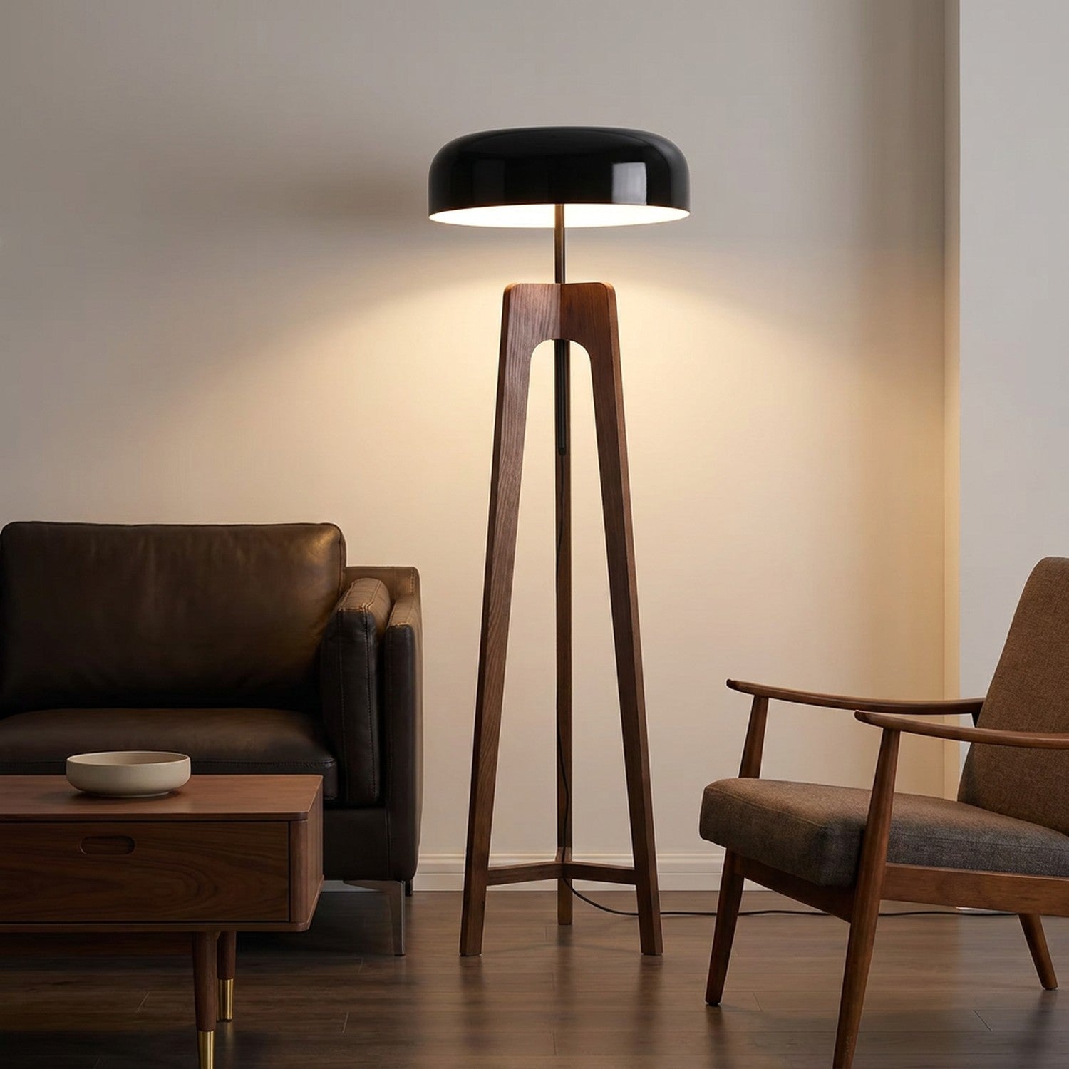 lampadaire trépied en bois foncé au dôme noir allumé près d'un canapé en cuir et d'un fauteuil