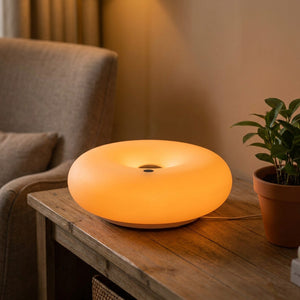 Lampe beignet Bauhaus allumée en orange dans un salon près d'une plante