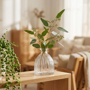 Vase en verre vintage à fines rainures avec des branches d eucalyptus sur une étagère en bois dans un salon lumineux