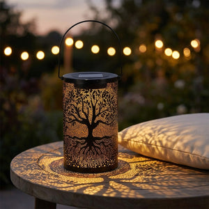 Lanterne solaire arbre de vie posée sur une table de jardin avec guirlande lumineuse en arrière-plan