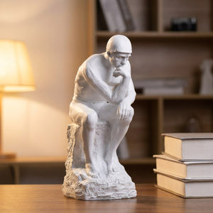 Statue Le Penseur de Rodin blanche sur un bureau avec des livres et une lampe chaleureuse
